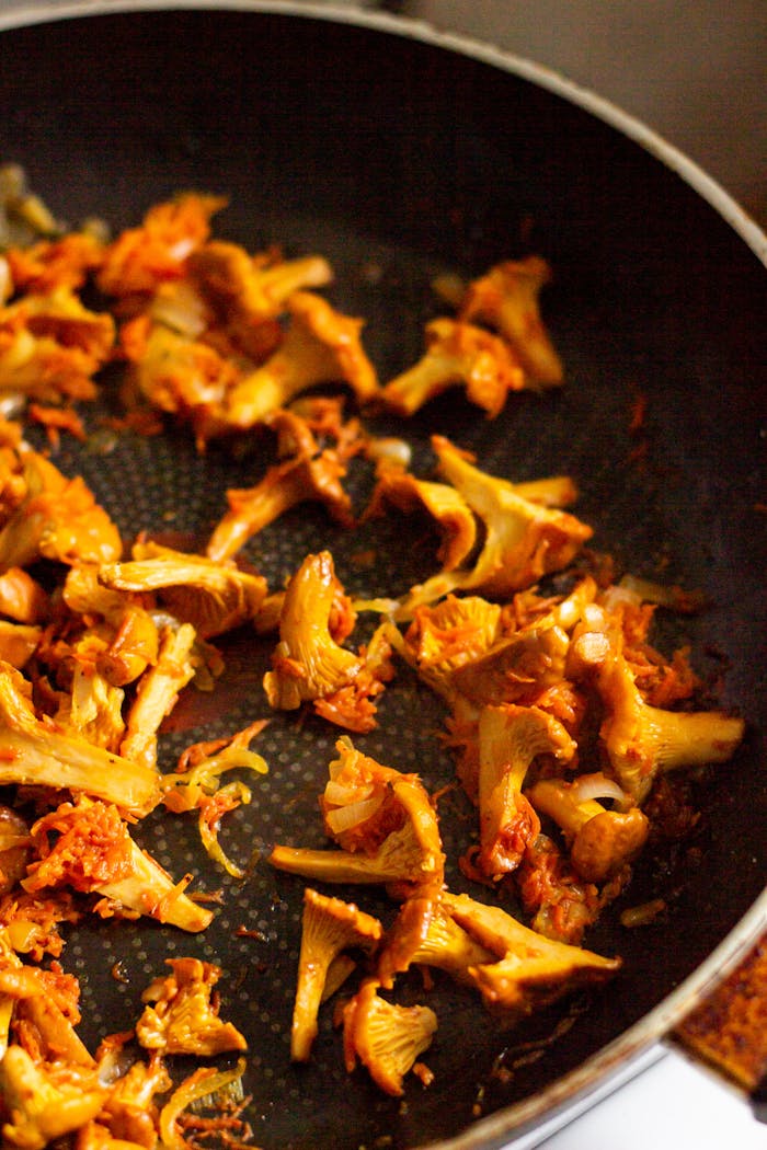 who-we-are Brightly colored chanterelle mushrooms sizzling in a frying pan, capturing the essence of fresh cooking.
